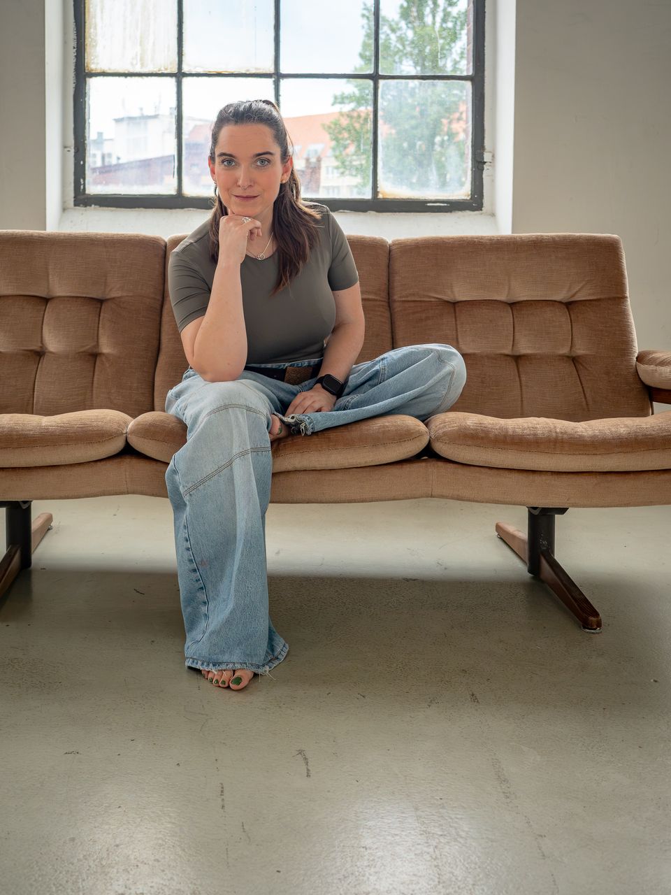 Miriam Göbel sitzt im Schneidersitz auf einem Sofa vor einem großen Fenster
