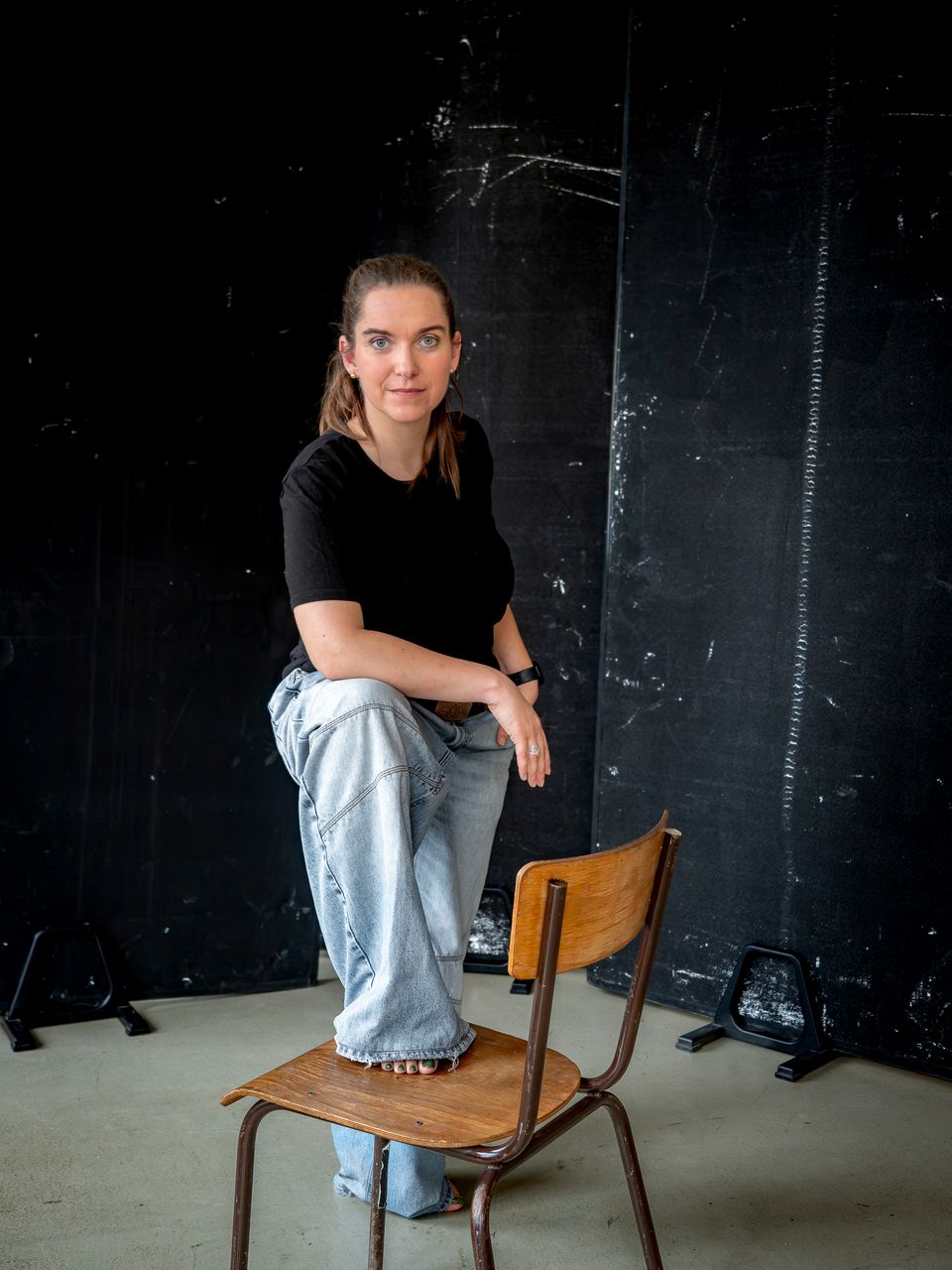 Miriam Göbel steht mit einem Fuß auf einem alten Holzstuhl vor dunklem Hintergrund